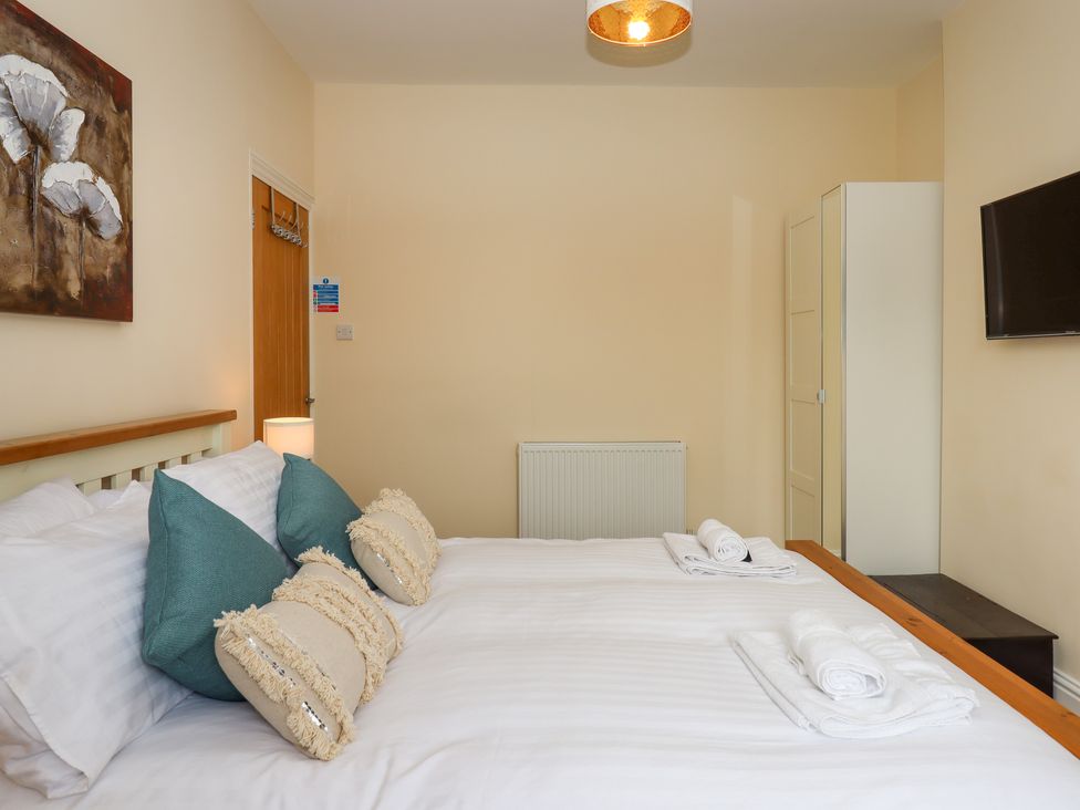 A bedroom with a bed with cushions and towels a wardrobe a television and a door at Rockland House in Brixham