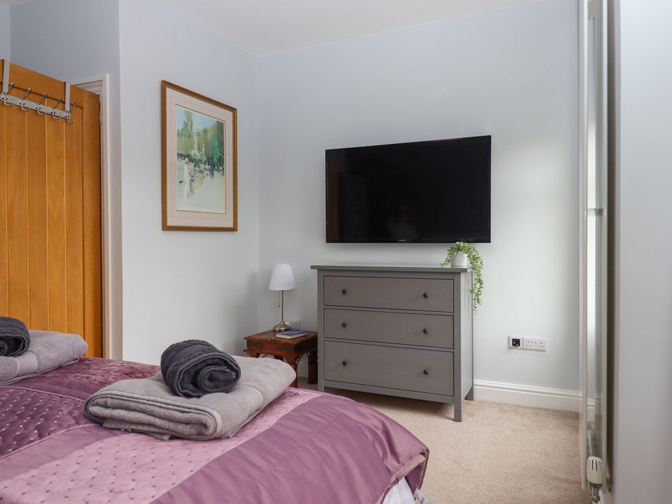A bedroom with a bed covered in a purple quilt and folded towels a gray dresser with a plant a wall-mounted television a wooden door and framed artwork at Rockland House in Brixham