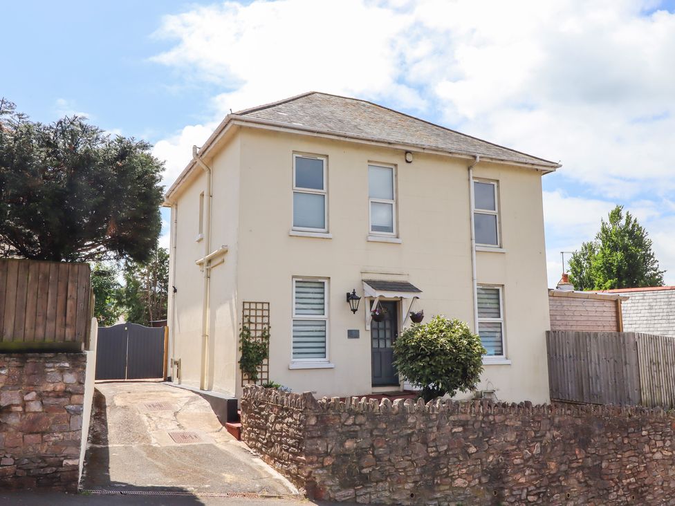 A two-story house with pale exterior walls and windows surrounded by a stone wall at Rockland House in Brixham