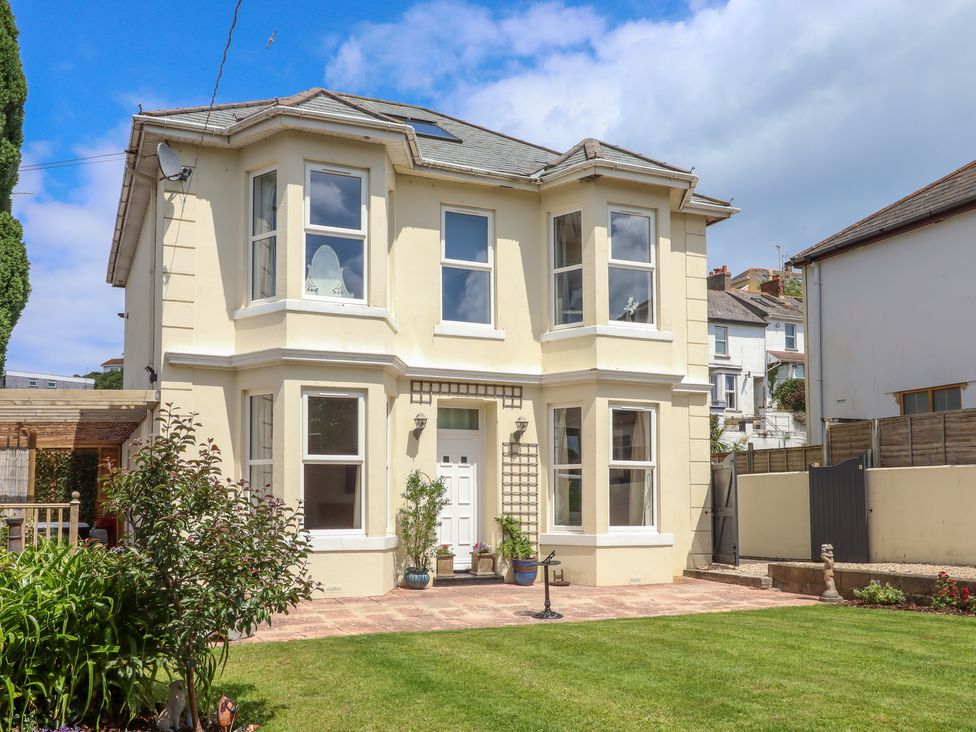A cream colored two story house with bay windows and a front garden at Rockland House in Brixham