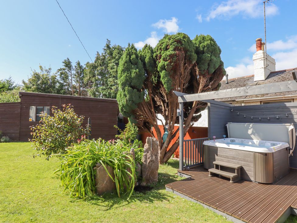 A backyard with a hot tub on a wooden deck surrounded by plants and trees at Rockland House in Brixham