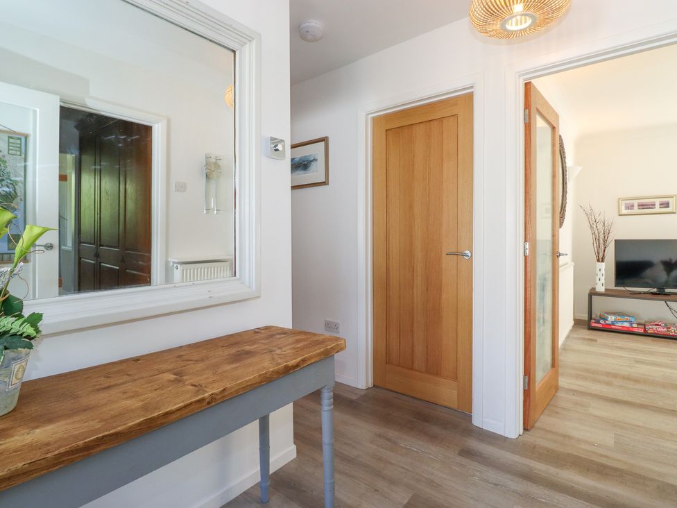 A hallway with a wooden table and a large wall mirror next to a closed wooden door and an open door leading to a living room at Sweden Bridge Cottage in Ambleside