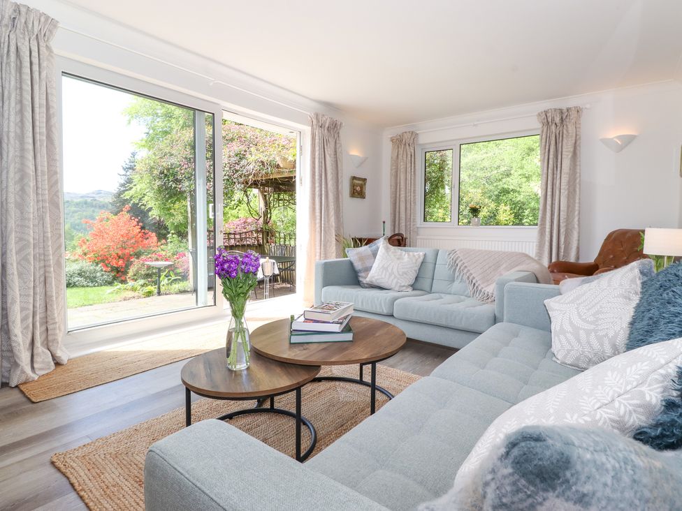 A living room with blue sofas and a wooden coffee table with books and flowers at Sweden Bridge Cottage in Ambleside