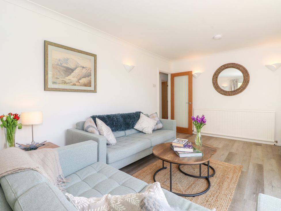 A living room with two sofas a round coffee table with books and flowers a wall mirror and a painting at Sweden Bridge Cottage in Ambleside