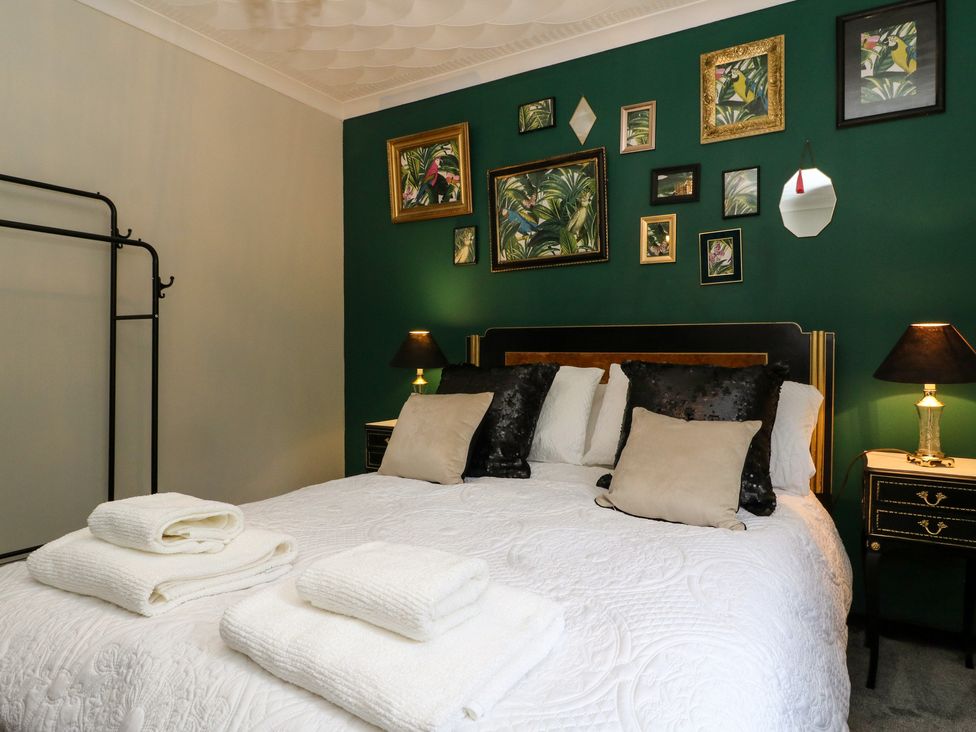 A bedroom with a bed covered with white bedding and pillows towels on the bed bedside tables with lamps and framed pictures on a green wall at Mo Dhachaidh in Roy Bridge