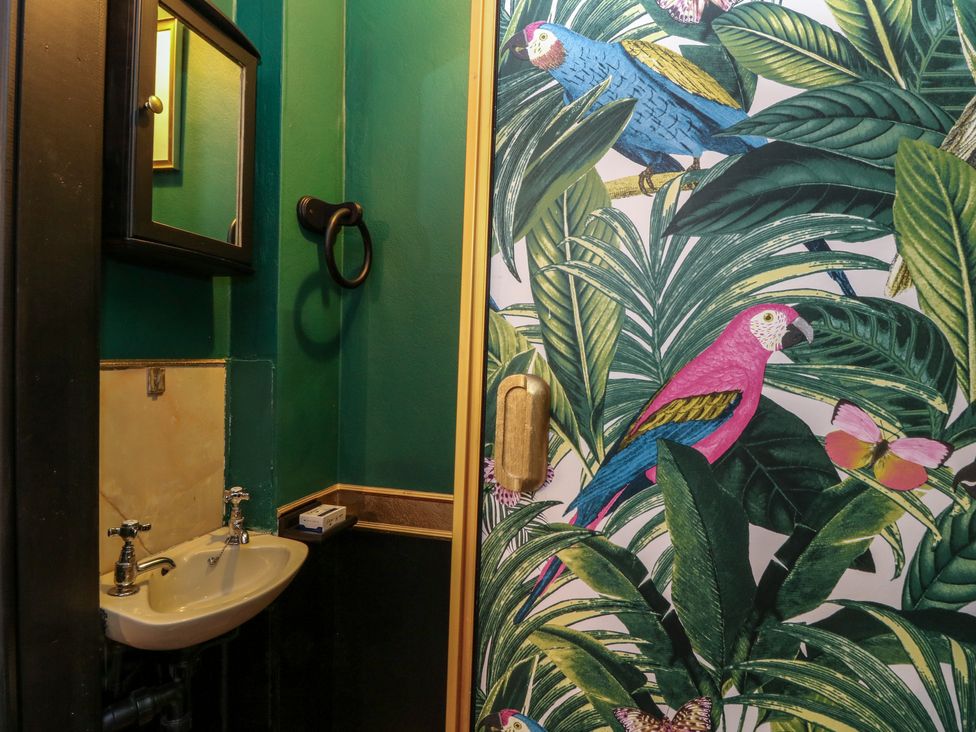 A small bathroom with green walls a white sink and a door with colorful bird and leaf patterns at Mo Dhachaidh in Roy Bridge