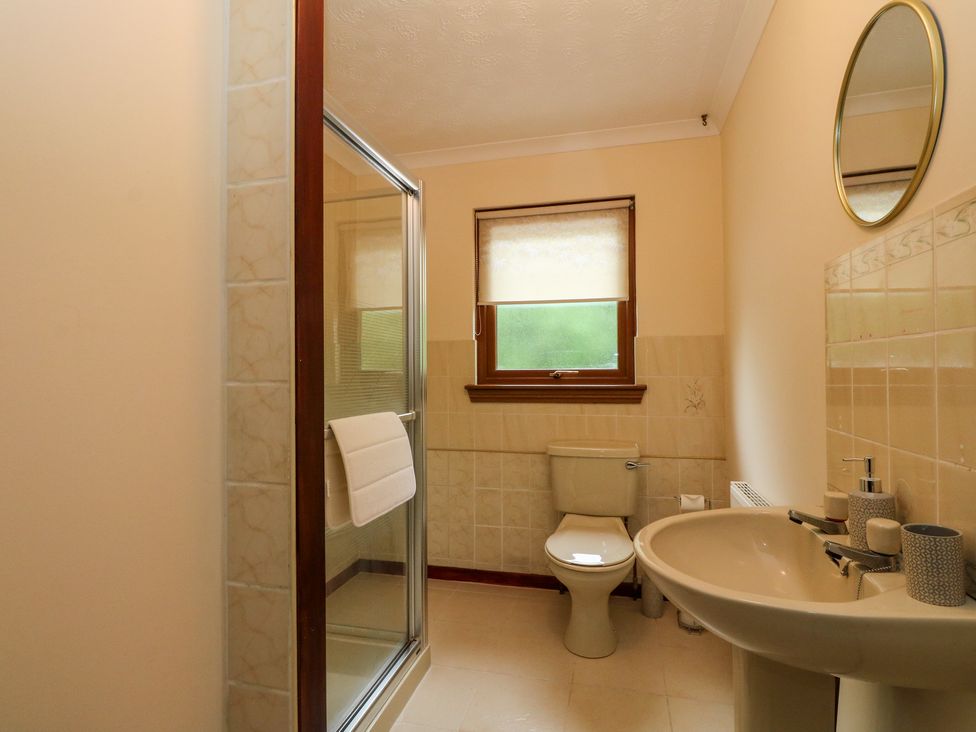 A bathroom with a shower enclosure a toilet a sink with toiletries and a round mirror at Mo Dhachaidh in Roy Bridge