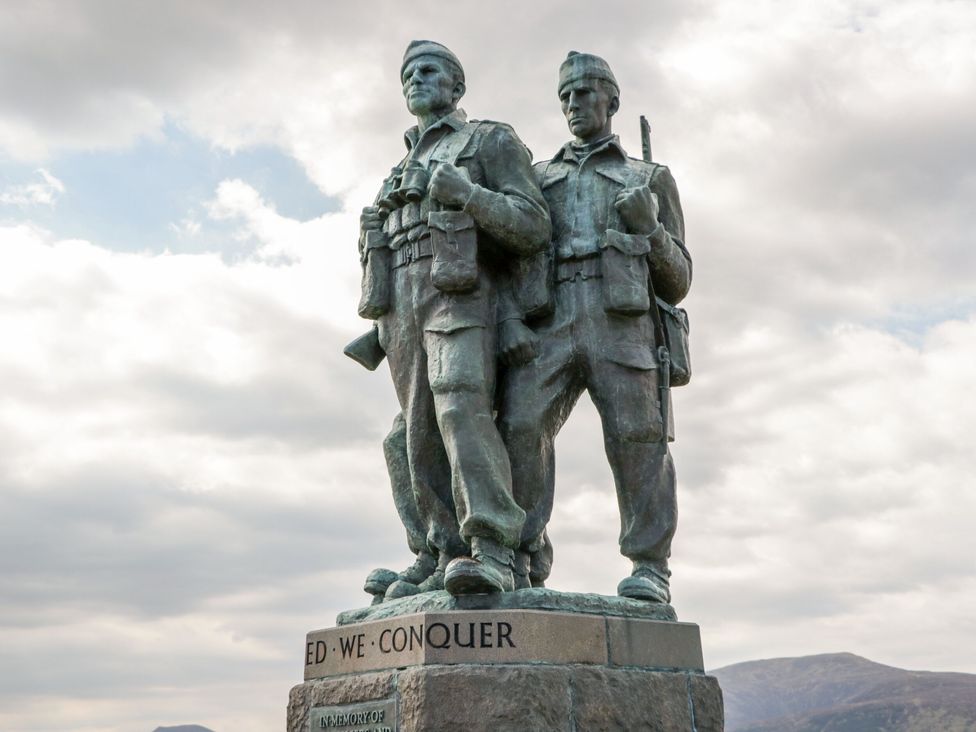 A statue of three soldiers standing on a stone pedestal with mountains in the background