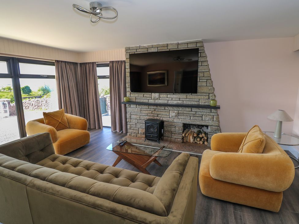 A living room with armchairs and sofa facing a stone fireplace with a mounted television at Cushranny in Mulranny County Mayo