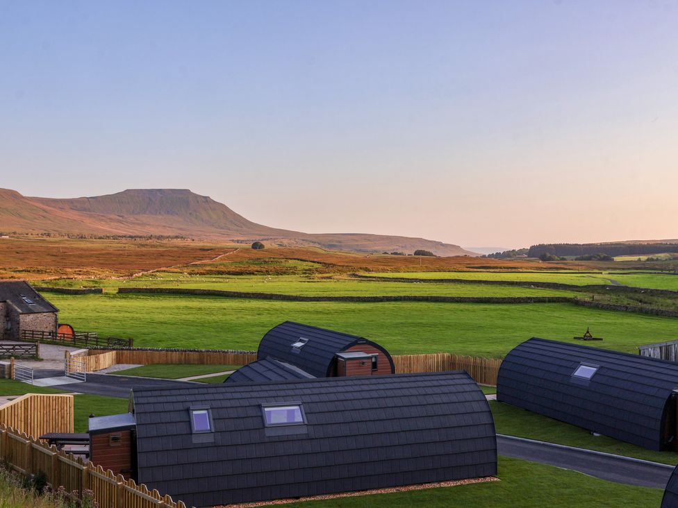 A rural landscape with curved black-roofed buildings green fields and mountains in the background at Barn Owl in Chapel Le Dale near Ingleton