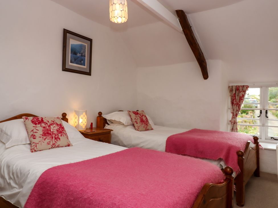 A bedroom with two single beds with pink blankets and floral cushions beside a window at Primrose Cottage in Drewsteignton