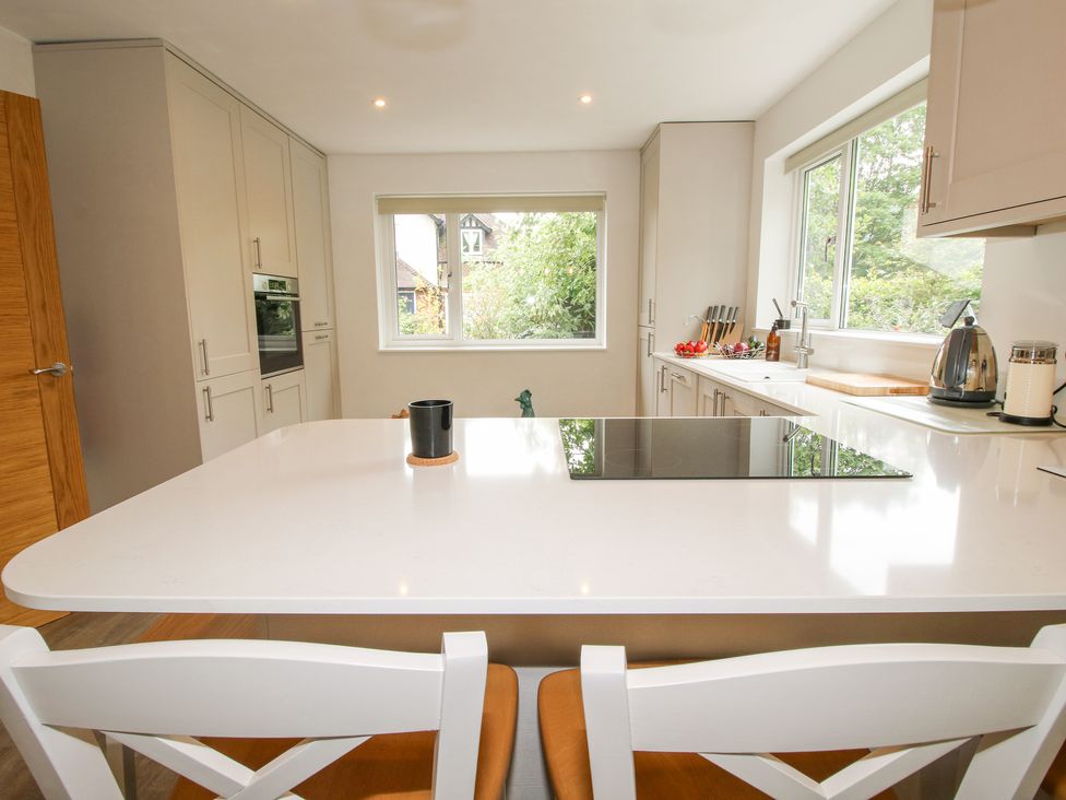 A kitchen with white cabinets a white island with stove and black cup two white chairs and windows showing greenery at 1 Church Street in Church Stretton