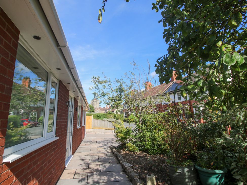 A path alongside a brick house with windows and door next to a garden with plants and trees at 1 Church Street in Church Stretton
