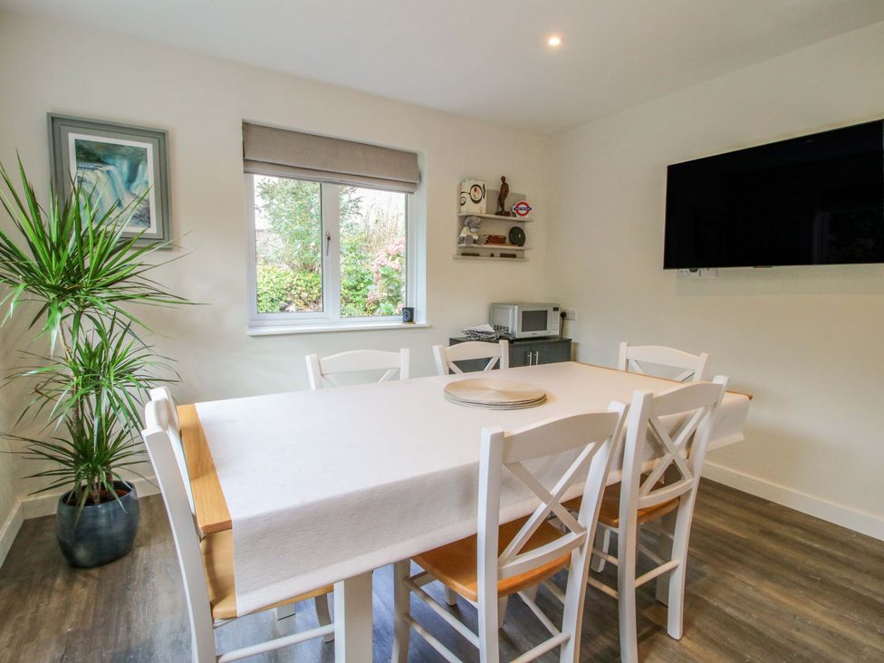 A dining room with a table covered by a white cloth and six chairs next to a window with a plant in the corner and a wall-mounted TV at 1 Church Street in Church Stretton