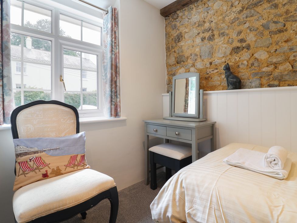 A small bedroom with a chair by a window a bed with towels and a dressing table against a stone wall at Myrtle Cottage in Uplyme