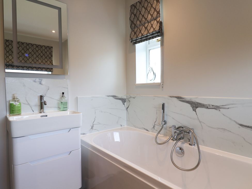 A bathroom with a bathtub sink mirror and window at Myrtle Cottage in Uplyme