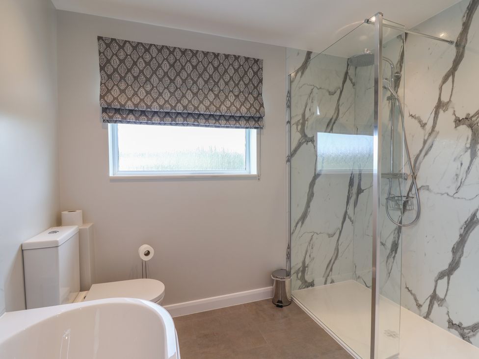 A bathroom with a toilet a bathtub a walk in shower and a window with a patterned blind at Myrtle Cottage in Uplyme