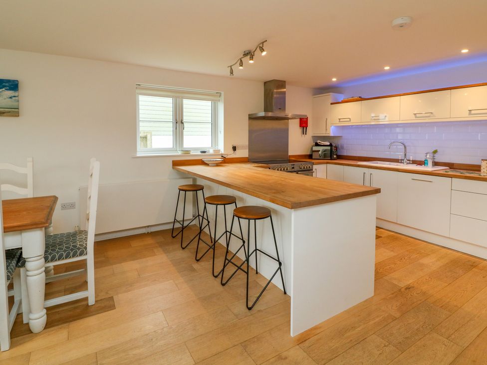 A kitchen with wooden countertops white cabinets a window and three bar stools at 9 Coastguard Cottages in Woolacombe