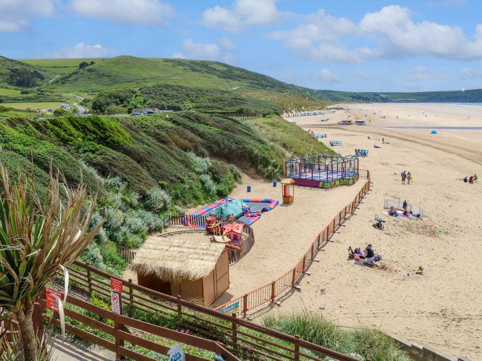 A sandy beach with a fenced children's play area and hills in the background at 9 Coastguard Cottages in Woolacombe