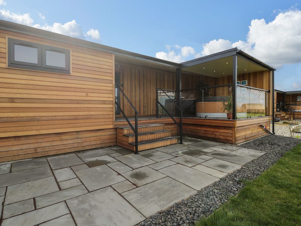 The exterior of a wooden lodge with steps leading to a covered porch with glass railings and a hot tub at Enia Lodge 2 in Llanelidan near Corwen