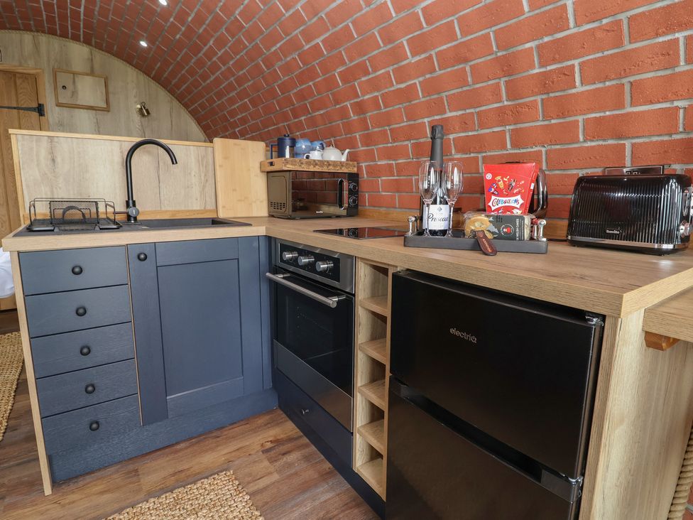A compact kitchen with blue cabinets wooden countertops a black fridge a toaster oven a microwave and a sink under a brick curved ceiling at Rhosydd Cyffylliog near Ruthin