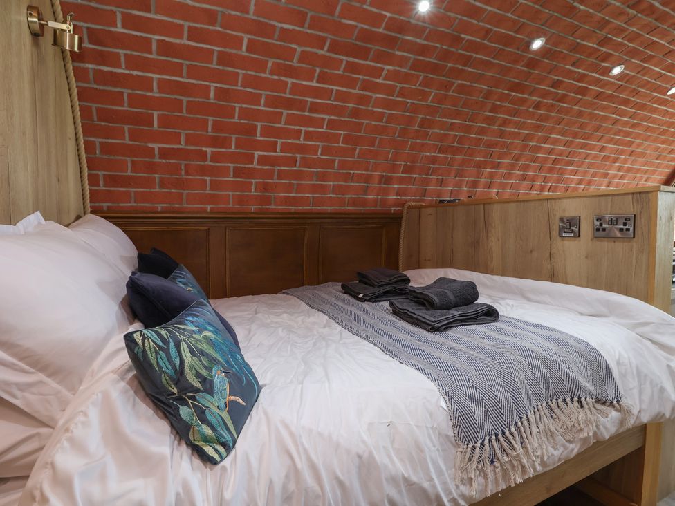 A bed with white sheets pillows and folded towels in a room with a curved brick wall at Rhosydd Cyffylliog near Ruthin
