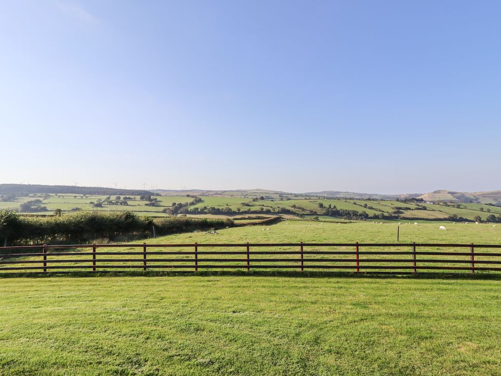 A grassy field with a wooden fence and rolling hills under a clear sky at Rhosydd in Cyffylliog near Ruthin