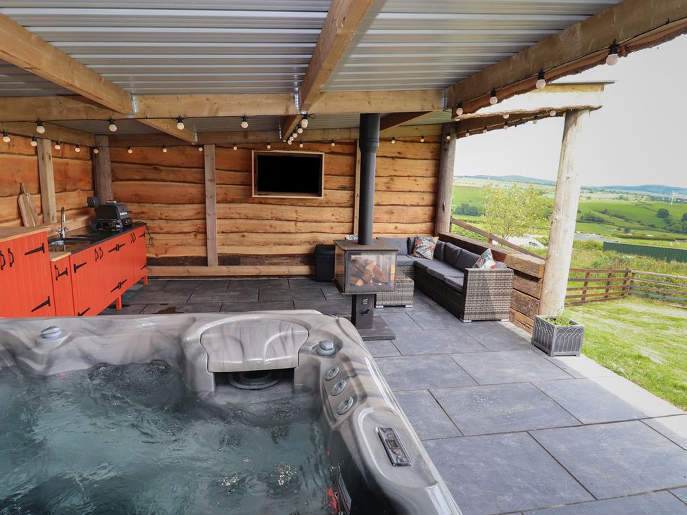 An outdoor covered patio with a hot tub seating area wood stove orange cabinets and a television at Cae Bach in Cyffylliog near Ruthin