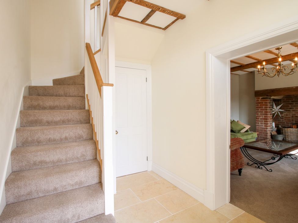A stairway with carpeted steps and a wooden handrail next to a closed white door and an open doorway leading to a living room with a glass coffee table at Daniels Farmhouse in Claines