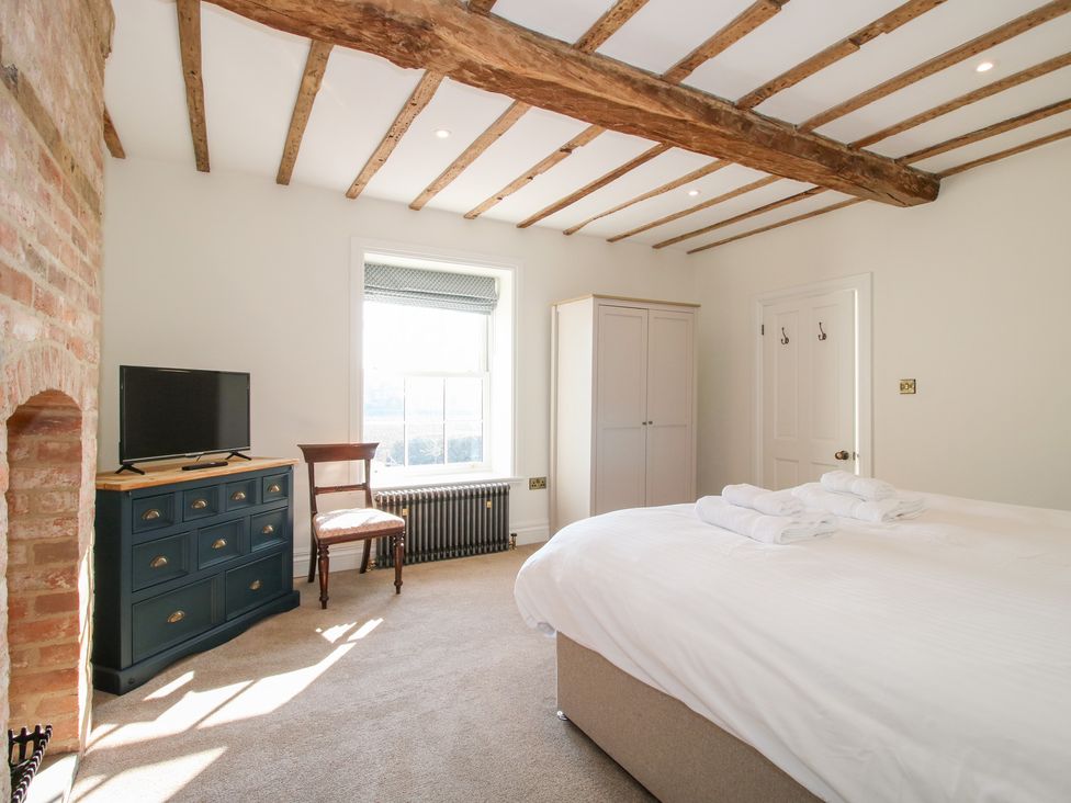 A bedroom with a bed set up with towels a wardrobe window chair a chest of drawers with a television and exposed wooden beams at Daniels Farmhouse in Claines