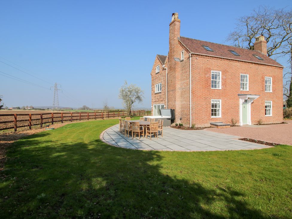 A brick house with multiple windows next to a patio with outdoor dining furniture and grass at Daniels Farmhouse in Claines