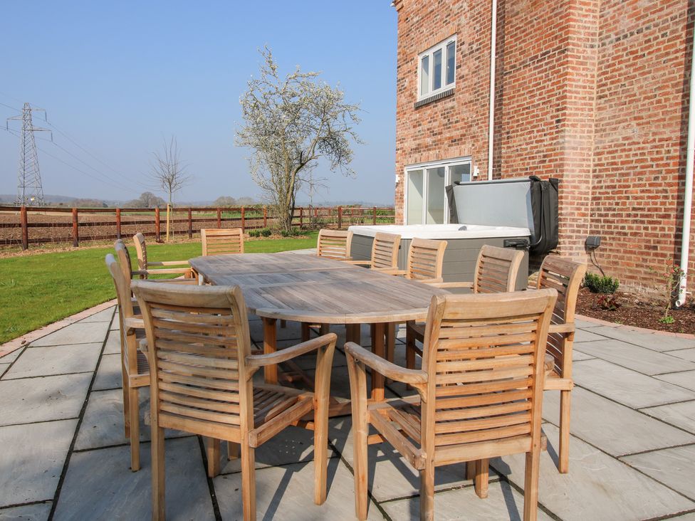 An outdoor patio with a wooden table and chairs next to a brick house and a hot tub at Daniels Farmhouse in Claines