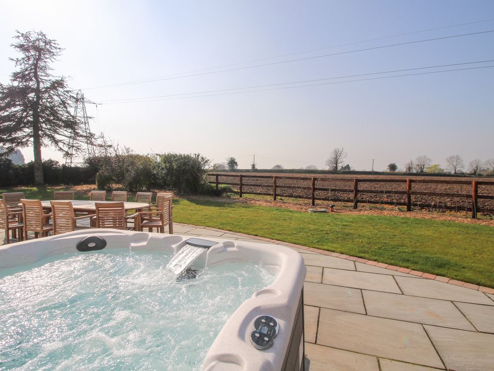 An outdoor patio with a hot tub and a wooden table with chairs overlooking a fenced field at Daniels Farmhouse in Claines