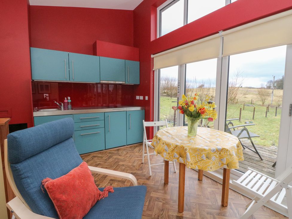 A kitchen area with teal cabinets a wooden table with yellow tablecloth a vase of flowers and a blue chair with red cushion at Tirlaggan Studio in Lismore