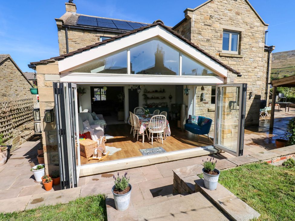 A patio with flower pots outside a stone house with an open conservatory showing a dining table and chairs at 14 Hill Close in Reeth
