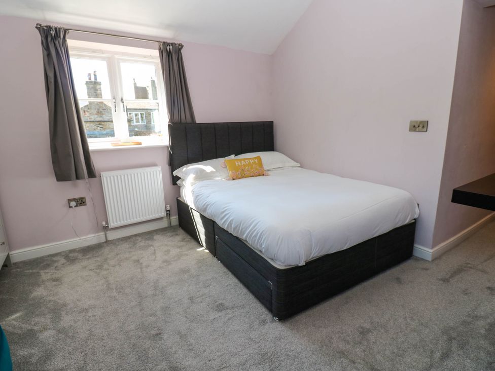 A bedroom with a double bed white bedding gray headboard gray curtains and a window at 14 Hill Close in Reeth