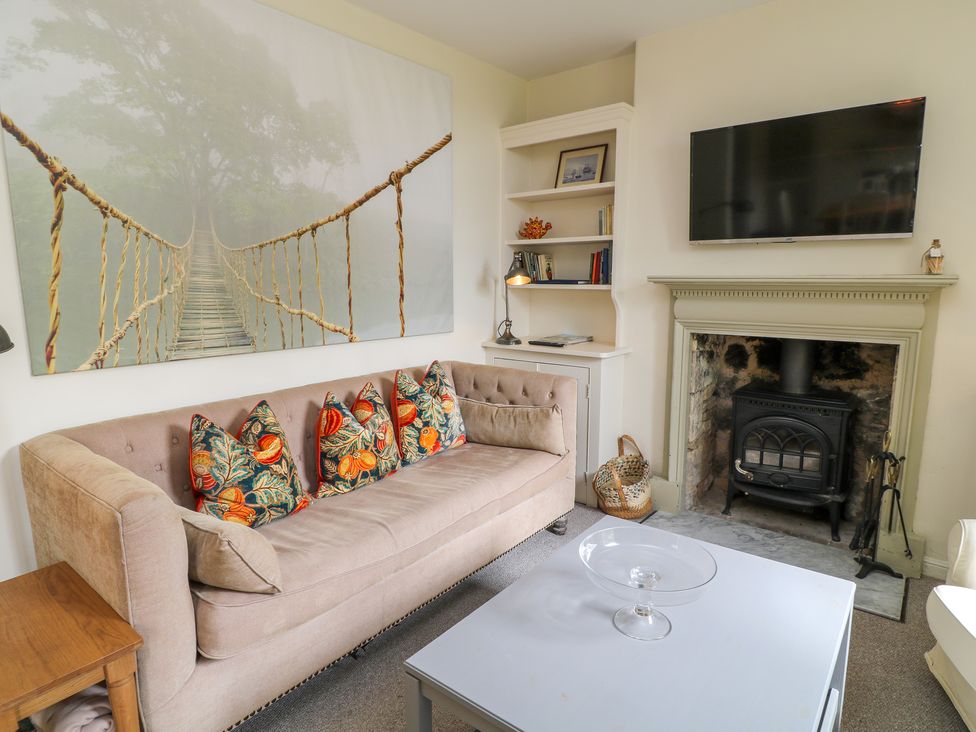 A living room with a beige sofa and patterned cushions a white coffee table a fireplace with a wood stove a mounted TV and built in shelves at Peartree in Colerne