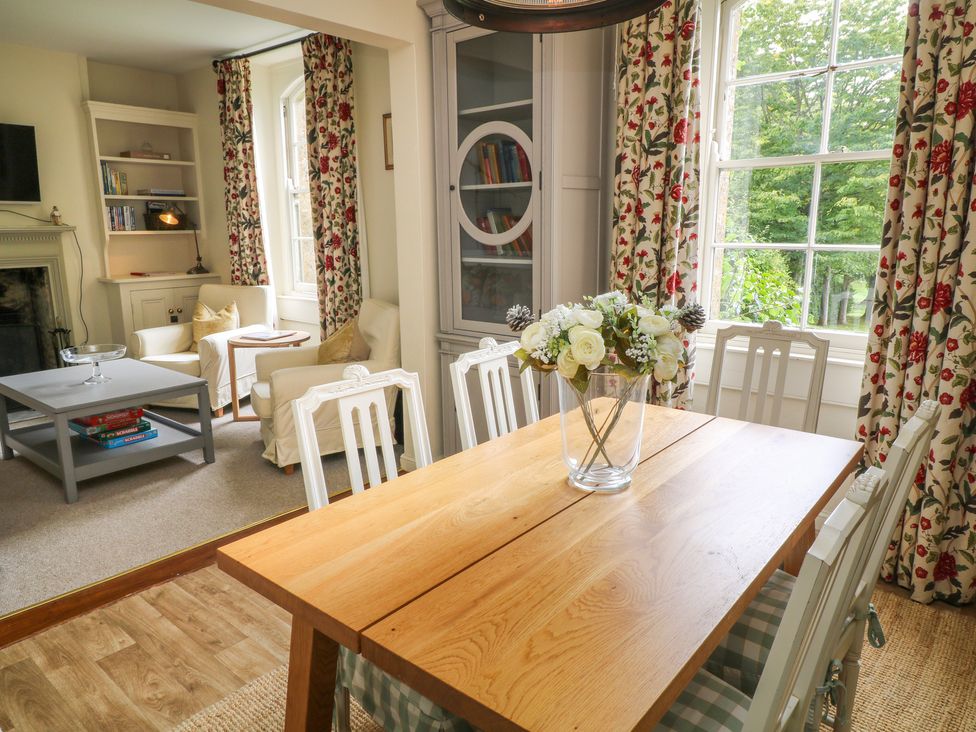 A dining room with a wooden table and white chairs next to a sitting area with armchairs and a coffee table at Peartree in Colerne
