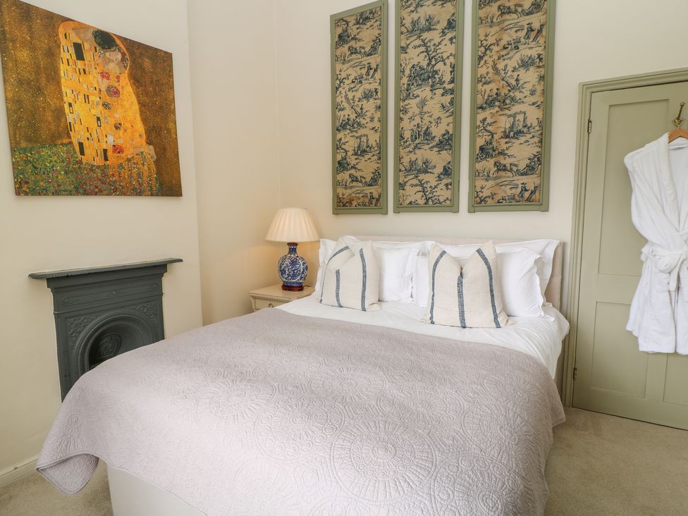 A bedroom with a bed covered in a quilt next to a side table with a lamp and decorative panels on the wall at Peartree in Colerne