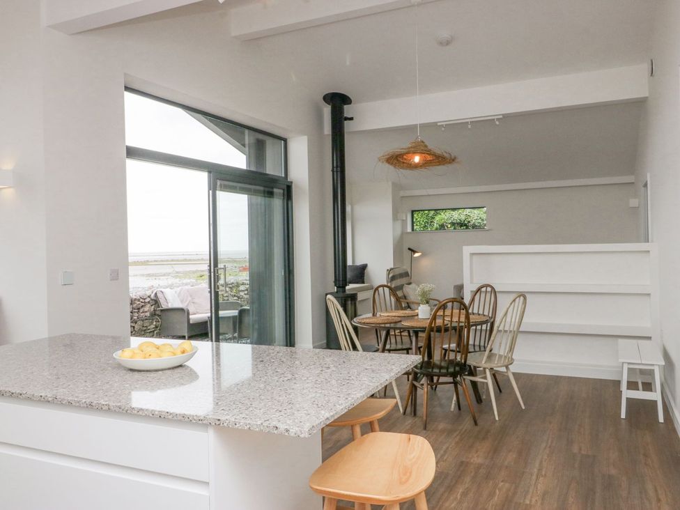 A dining area with a round table and mixed chairs next to a kitchen island and large sliding glass doors at Driftwood Cottage in Ulverston