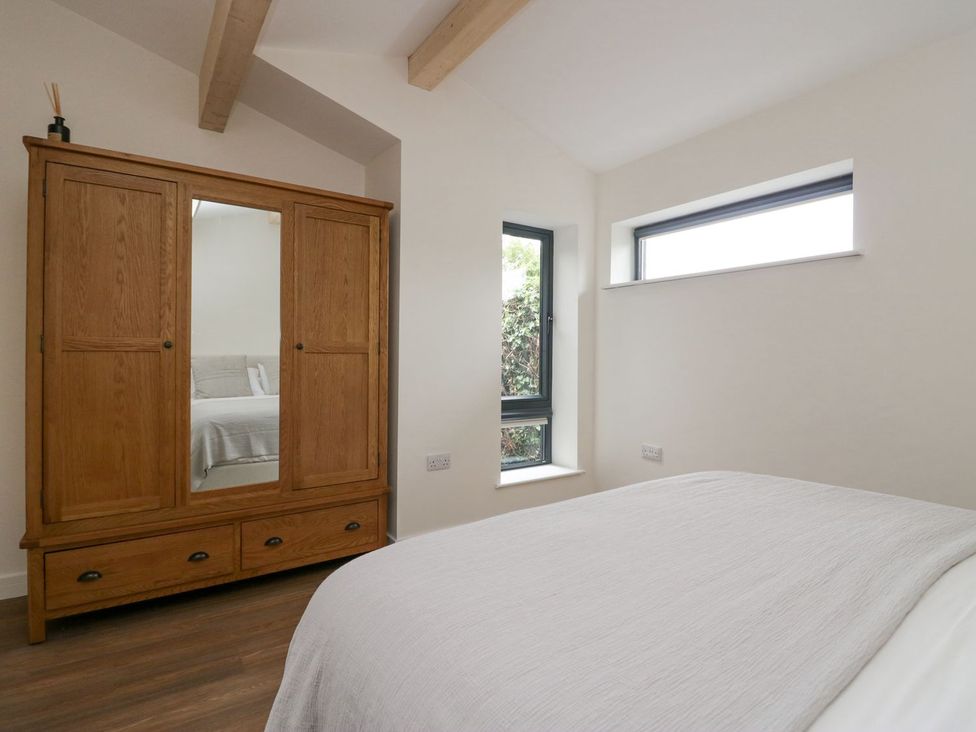 A bedroom with a wooden wardrobe and two windows at Driftwood Cottage in Ulverston