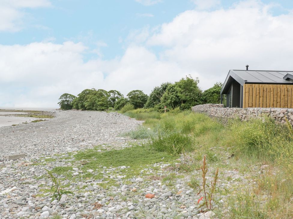 A rocky coastline with grass and bushes beside a wooden and stone house at Driftwood Cottage in Ulverston