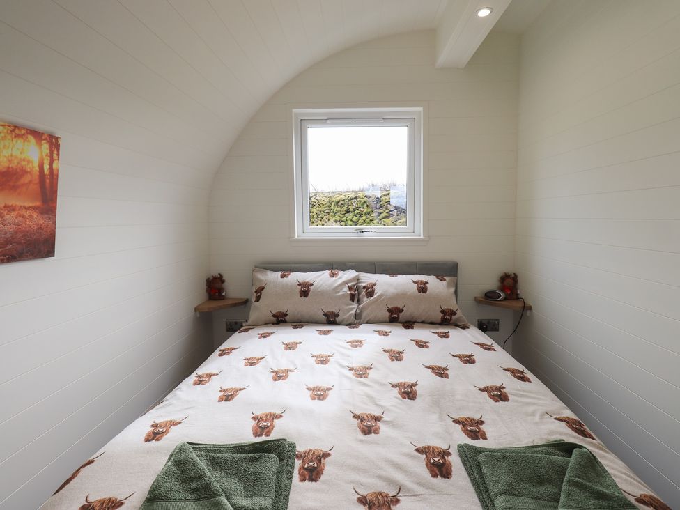 A bedroom with a bed featuring animal print bedding green towels on the bed and a window above the headboard at Shepherds View in Castlerigg near Keswick