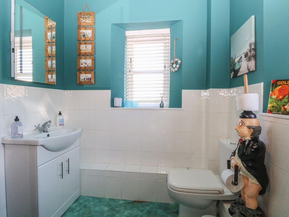 A bathroom with a white sink and cabinet a toilet a window with blinds and blue walls at Cobble Cottage in Great Ryburgh