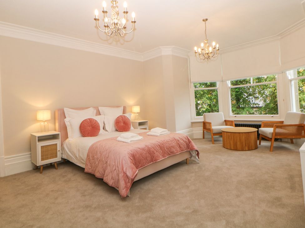 A bedroom with a double bed two bedside tables with lamps two armchairs and a round wooden table by windows at Spa House in Buxton