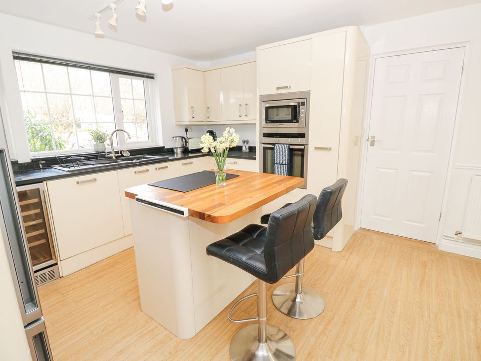 A kitchen with a wooden countertop island and black stools by a window at Bay Cottage in Bembridge
