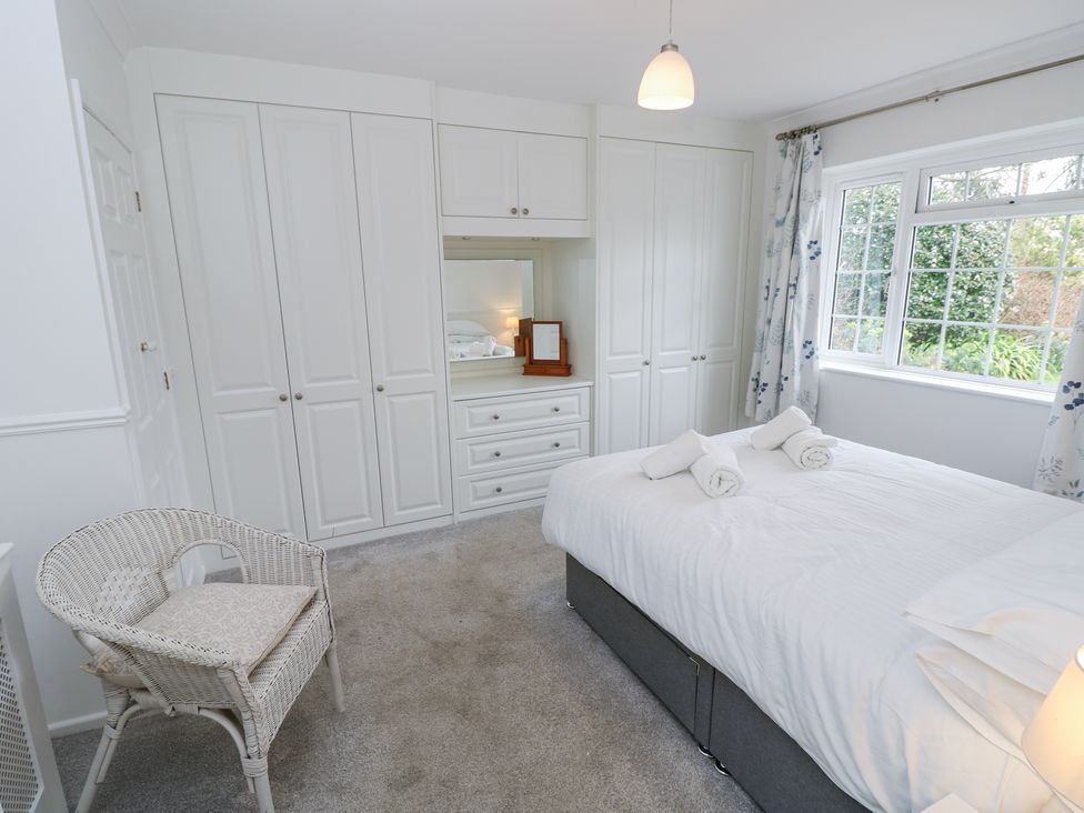 A bedroom with white wardrobes a bed with rolled towels a wicker chair and a window at Bay Cottage in Bembridge