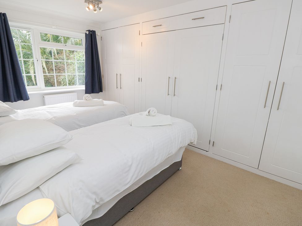 A bedroom with two single beds white wardrobes and a window with curtains at Bay Cottage in Bembridge