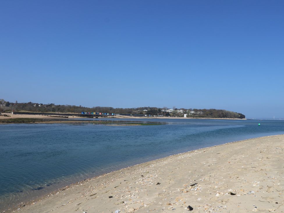 A sandy beach with a body of water and a distant shoreline with buildings and trees at Bay Cottage in Bembridge