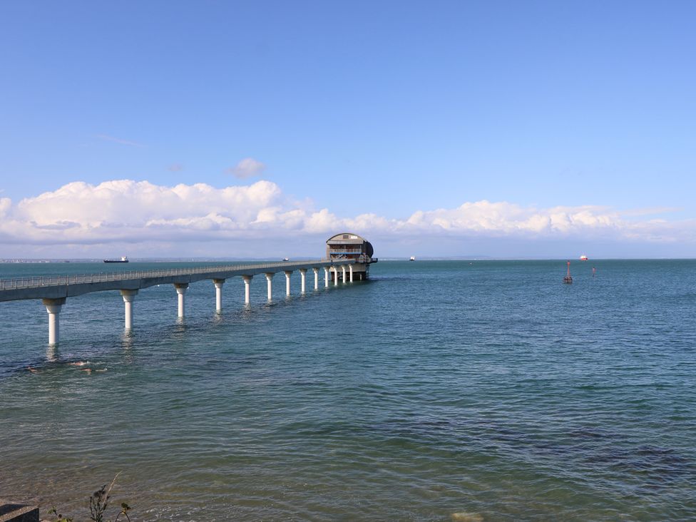 A long concrete pier with a building at the end extending into the sea with ships in the distance at Bay Cottage in Bembridge